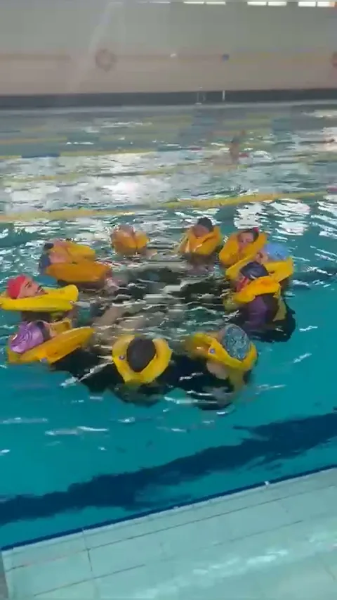 Alumnos con chalecos salvavidas formando un grupo durante las prácticas de piscina